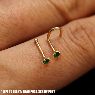 Close up view of a single two Emerald Gemstone Nose Studs with different backings resting on the back on a model's hand