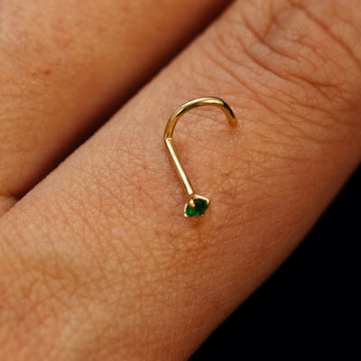 Close up view of a single 14k solid gold emerald Gemstone Nose Stud with screw post resting on the back on a model's hand