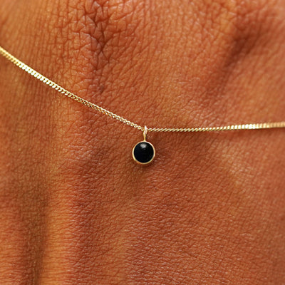 Close up view of a 14k yellow gold Onyx Necklace draped across the back of a model's hand