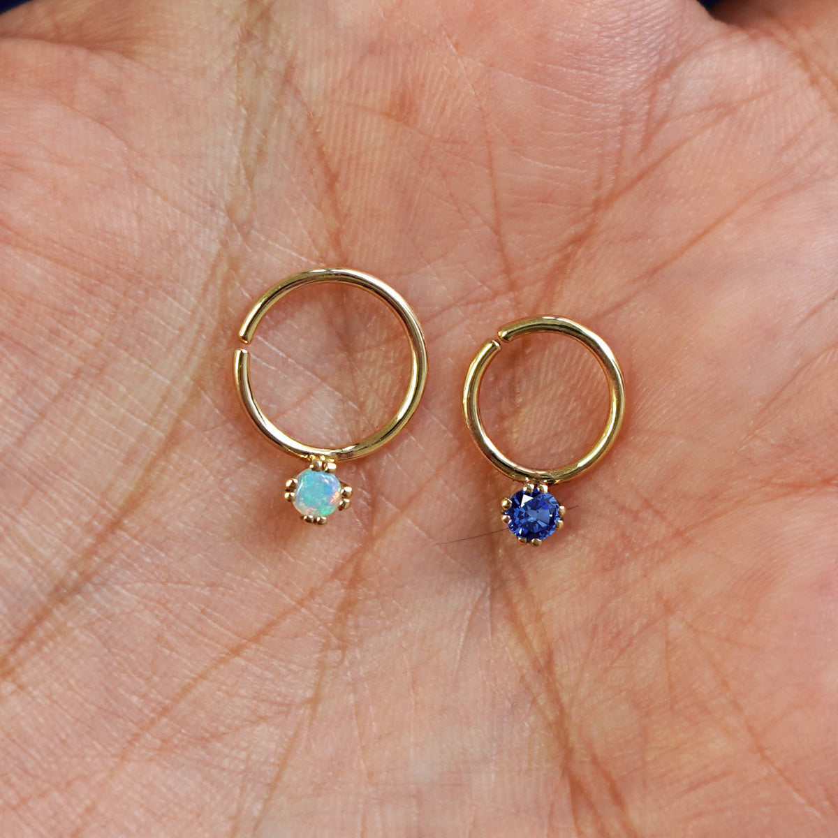 A 10mm opal pierced septum and an 8mm sapphire pierced septum resting in a model's palm