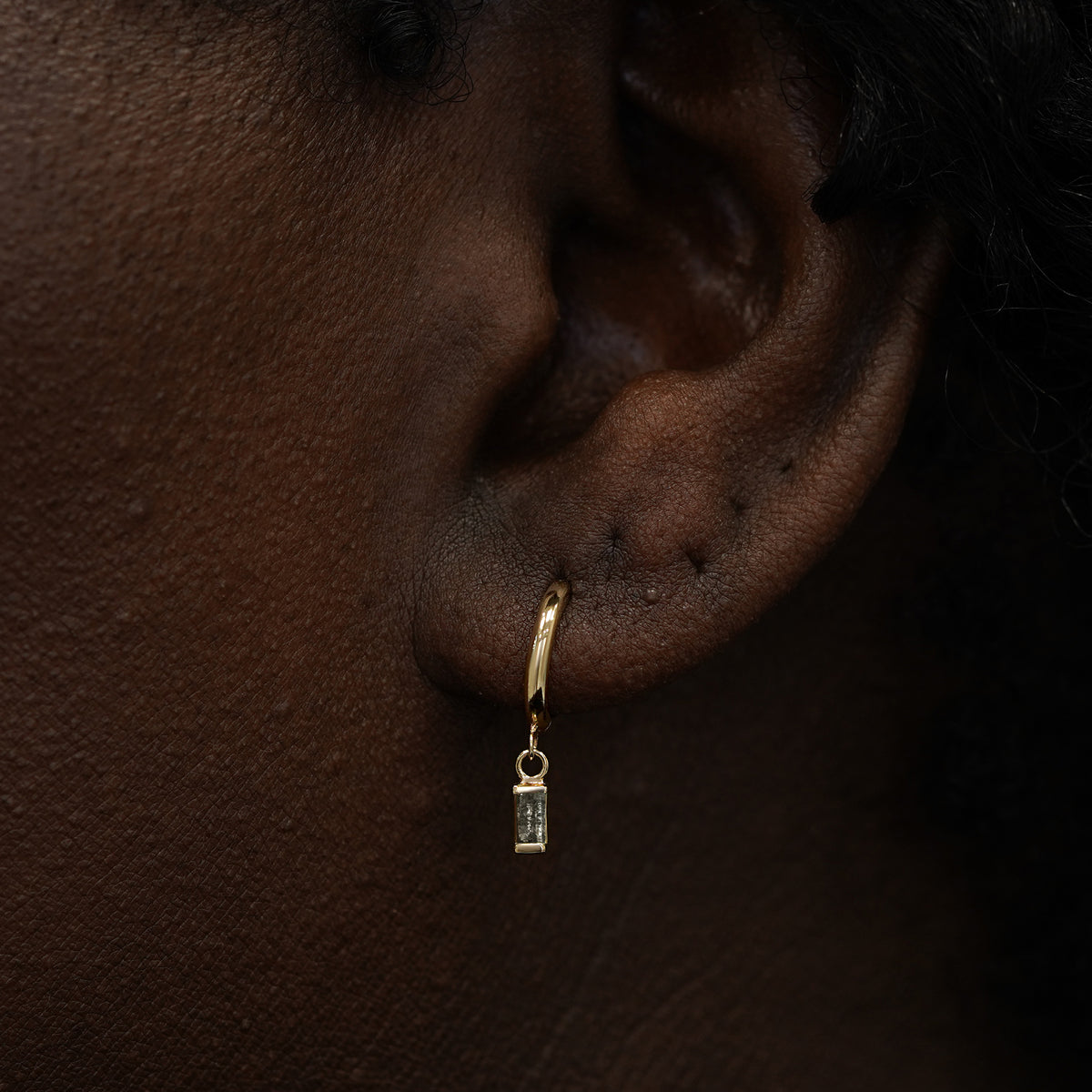 A model wearing a solid 14k gold baguette salt and pepper diamond charm hoop earring
