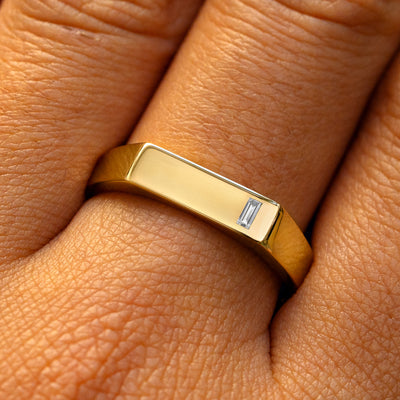 A model's finger wearing a yellow gold baguette natural or lab diamond rectangular signet ring