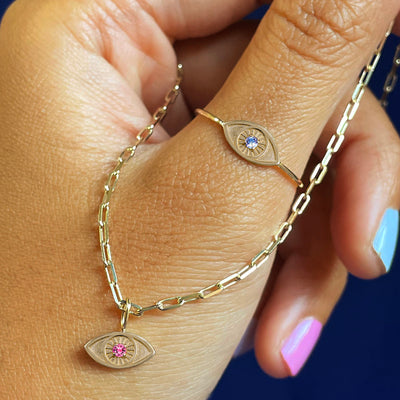 A hand wearing a Gemstone Evil Eye Ring holding an Butch Chain with a gemstone evil eye charm 