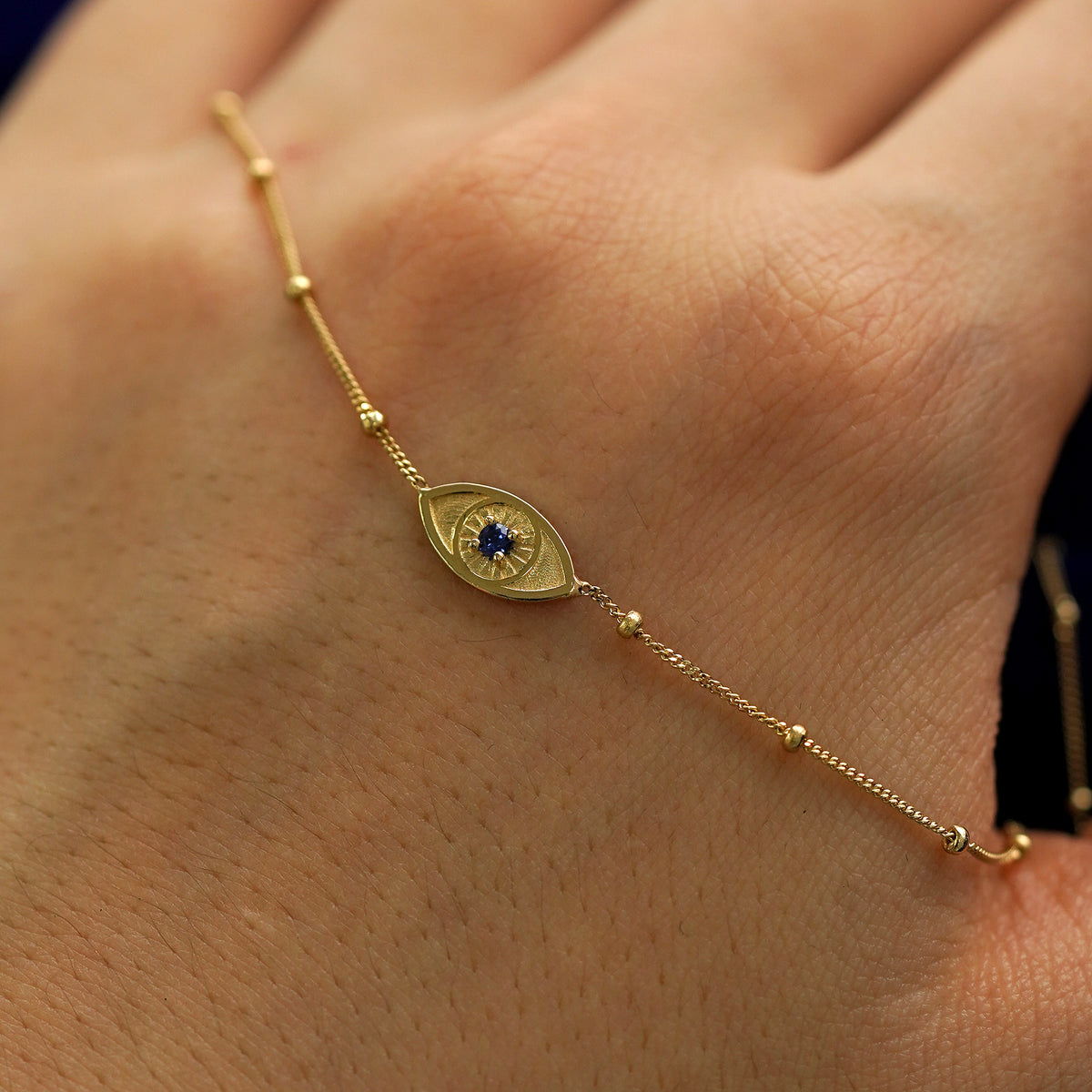 A solid gold gemstone evil eye bracelet draped across the back of a model's hand