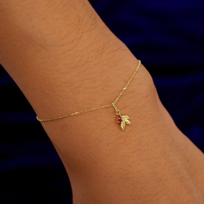 A model's wrist wearing a yellow gold ruby Gemstone 3 Leaves Charm on a Cable Bracelet