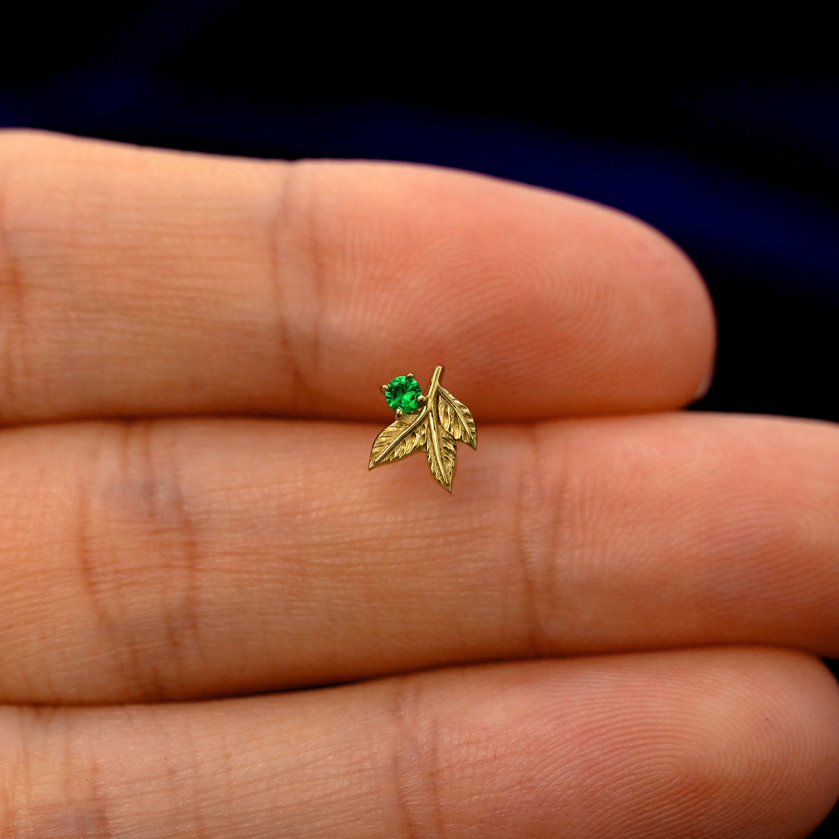 A model holding a solid gold emerald 3 Leaves Gemstone stud earring between two fingers