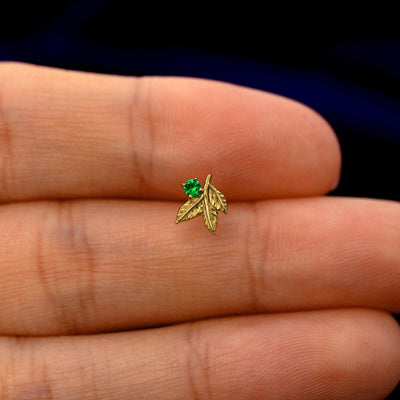 A model holding a solid gold emerald 3 Leaves Gemstone stud earring between two fingers