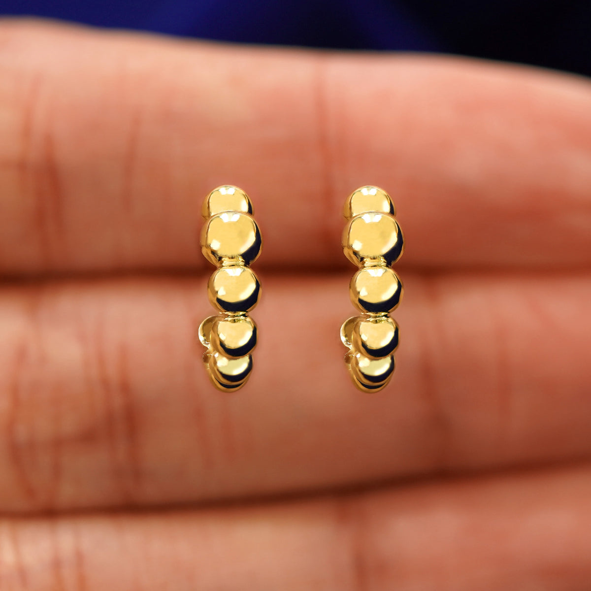 A model's hand holding a pair of 14k yellow gold Graduated Puffy Beaded Hoops in between their fingers