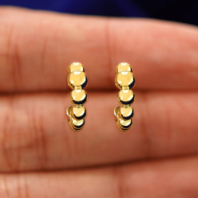 A model's hand holding a pair of 14k yellow gold Graduated Puffy Beaded Hoops in between their fingers