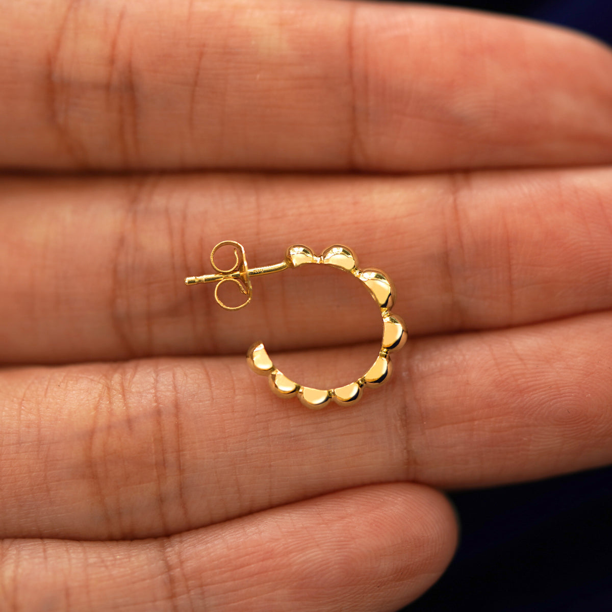 A Graduated Puffy Beaded Hoop laying sideways on a model's fingertips to show the details of the post and the side of the hoop