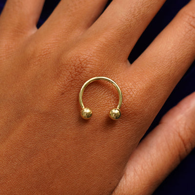 A yellow gold large horseshoe piercing resting on the back of a model's hand to indicate size