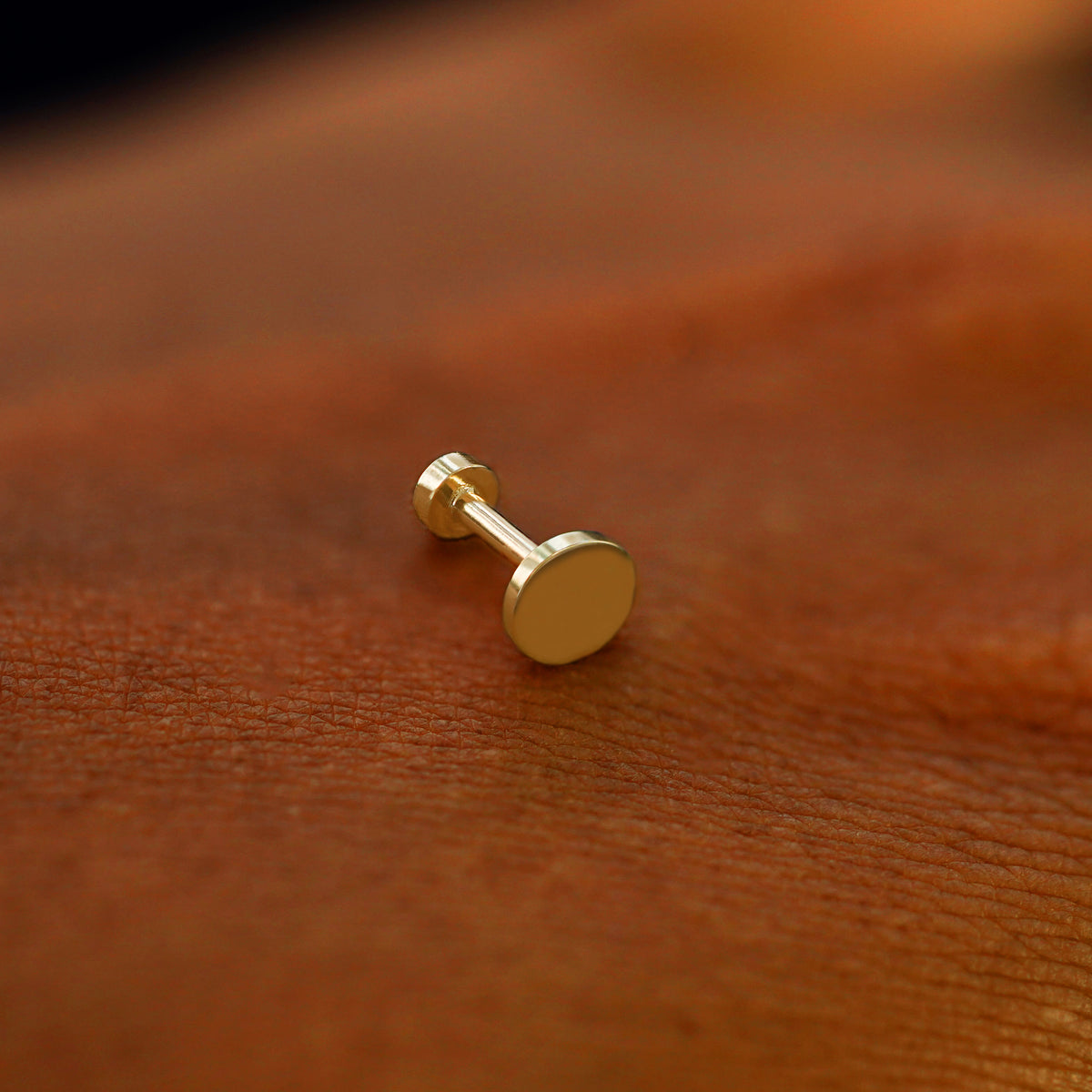 A solid 14k yellow gold Large Circle Flatback Piercing resting on the back of a model's hand
