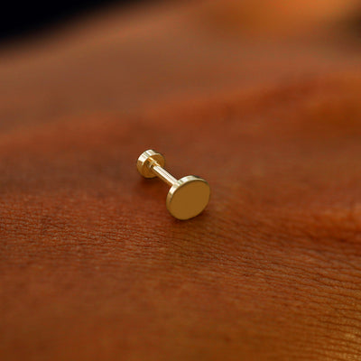 A solid 14k yellow gold Large Circle Flatback Piercing resting on the back of a model's hand