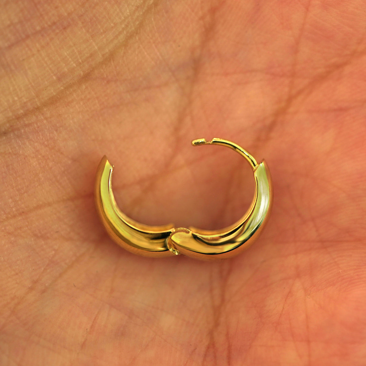 An open 14k yellow gold Medium Teardrop Huggie Hoop resting in a model's palm