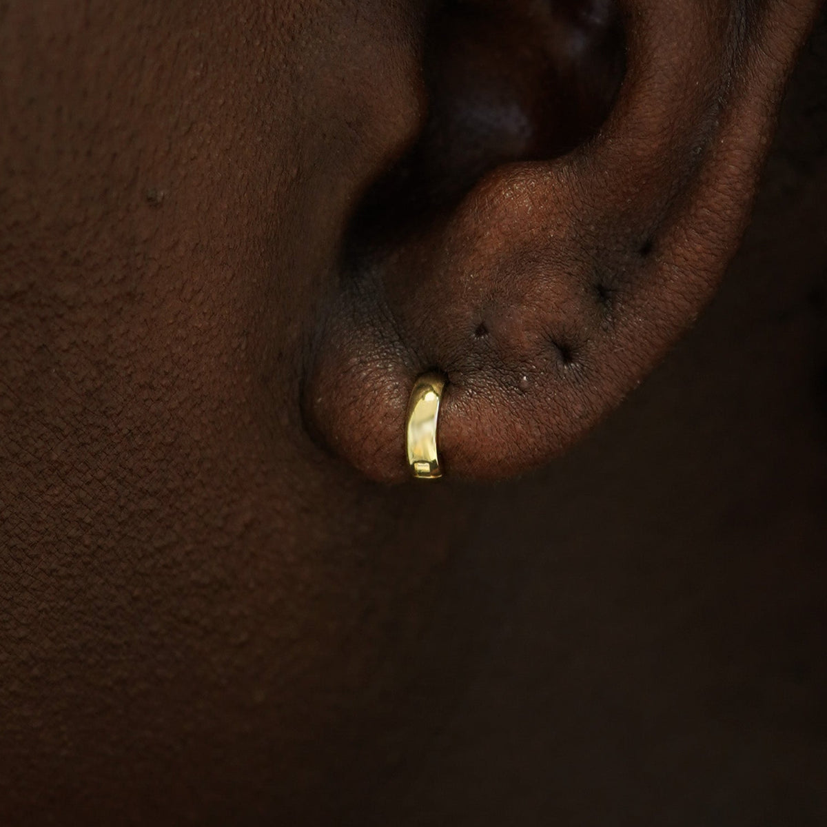 A model's ear wearing a 14k gold Mini Thick Huggie Hoop Earring