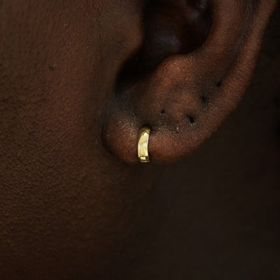 A model's ear wearing a 14k gold Mini Thick Huggie Hoop Earring