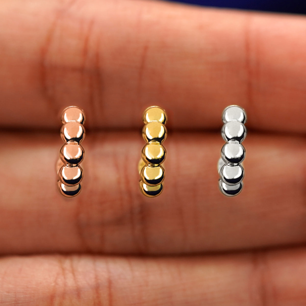 A model's hand holding three Mini Puffy Beaded Hoops in between their fingers in rose, yellow, and white gold