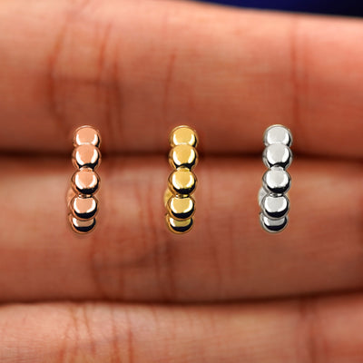 A model's hand holding three Mini Puffy Beaded Hoops in between their fingers in rose, yellow, and white gold