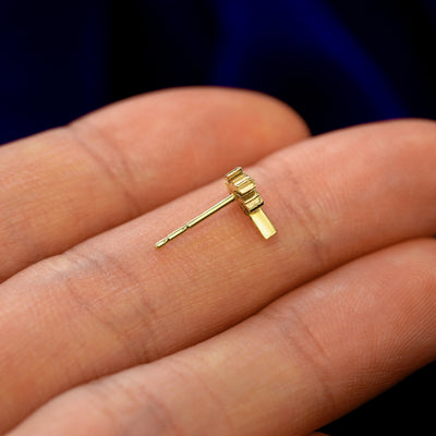 A 14k gold Palm Tree Earring in a model's hand resting on its side to show the thickness of the earring 