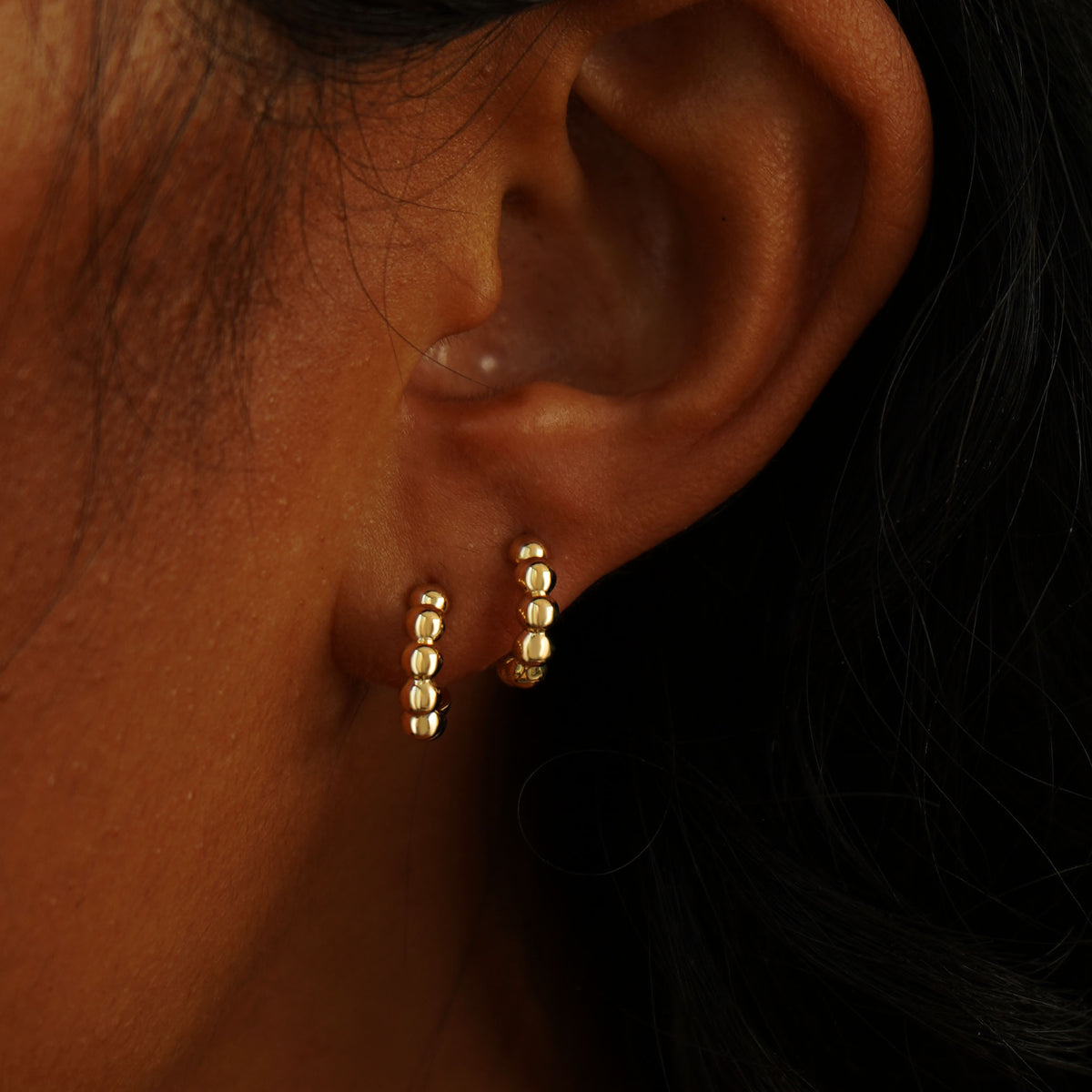 A model's ear wearing two yellow gold Mini Puffy Beaded Hoops in two separate lobe piercings