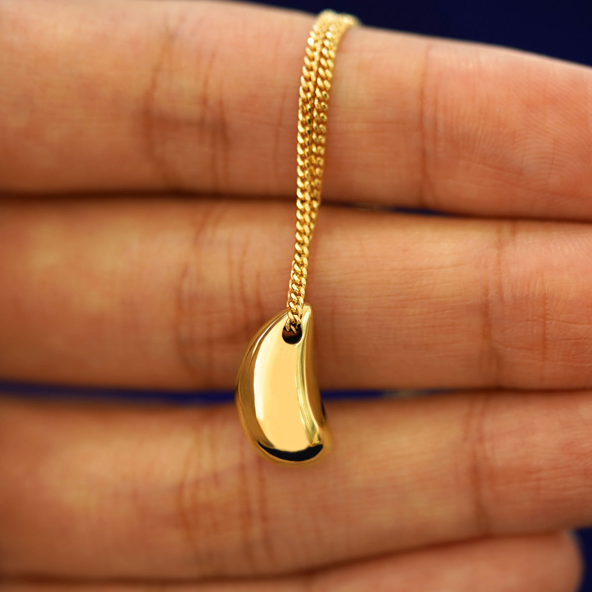 A Puffy Teardrop Necklace laying over a model's fingertips to show the details of the side view