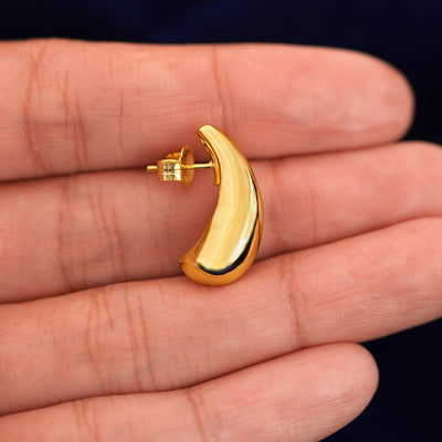 An Teardrop Puffy Earring laying sideways on a model's fingertips to show the details of the post and the side of the stud