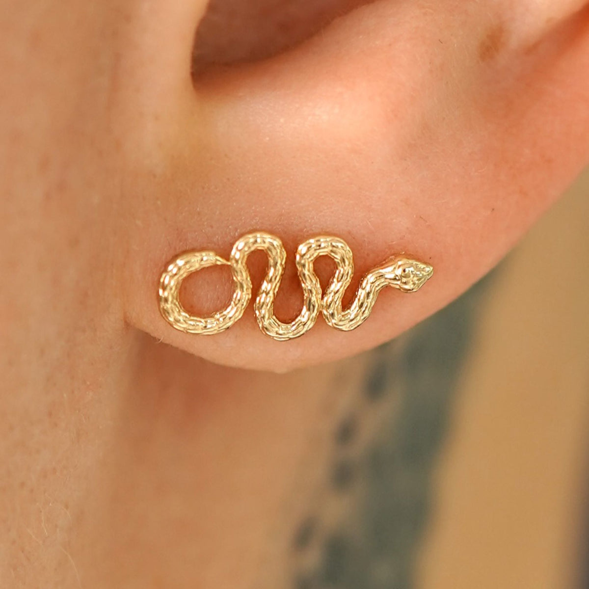 Close up view of a model's ear wearing a 14k gold Snake Earring with the snake horizontal