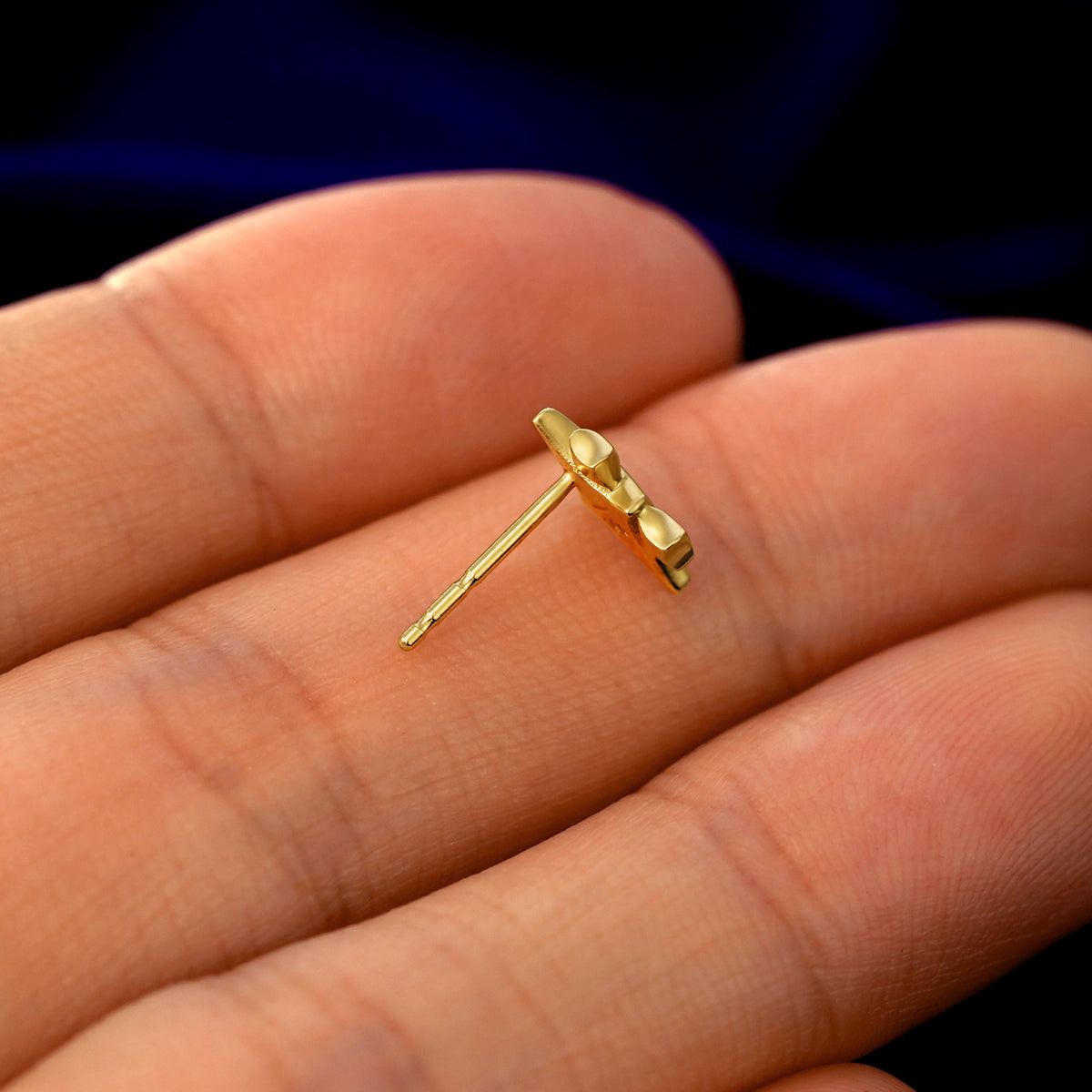 A 14k gold Sparkly Emoji Earring in a model's hand resting on its side to show the thickness of the earring 