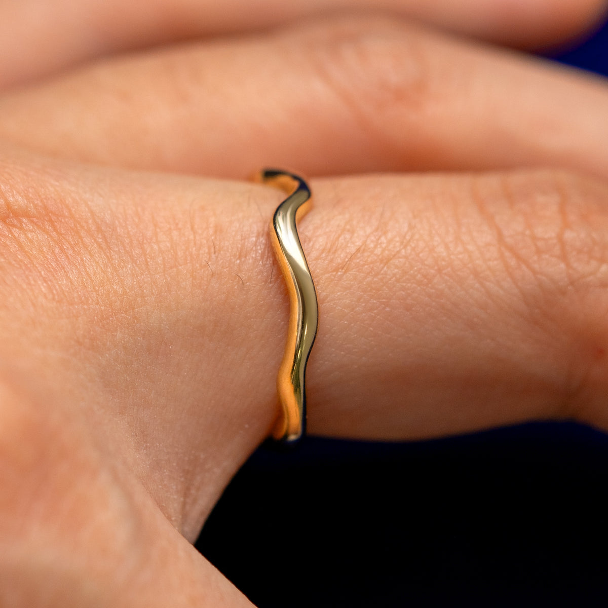 Side view of a solid 14 karat gold thin waved wedding band on a model's finger
