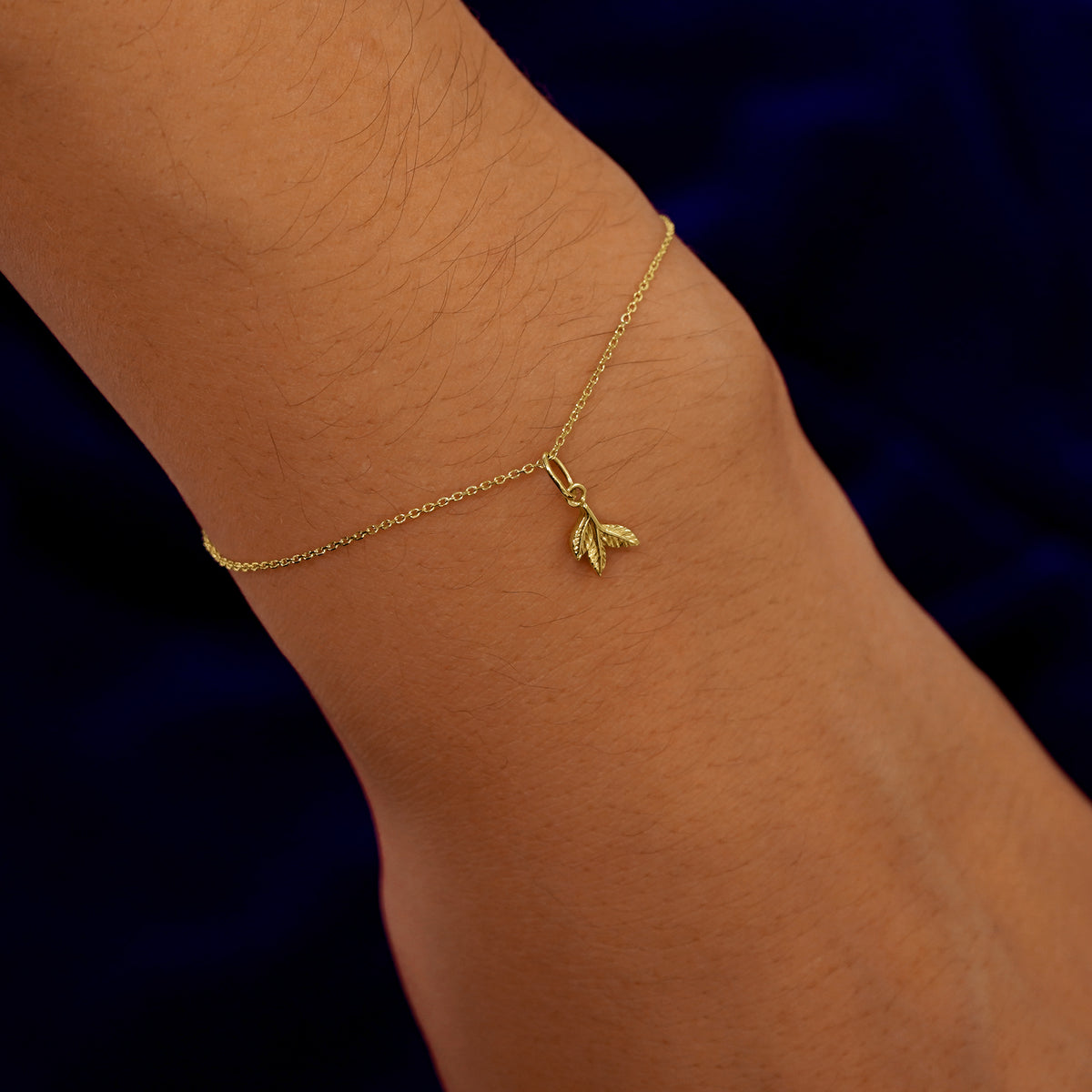 A model's wrist wearing a yellow gold 3 Leaves Charm on a Cable Bracelet
