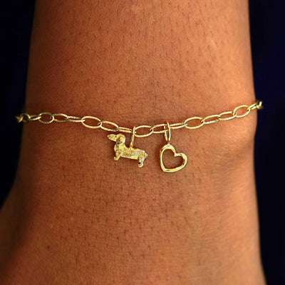 A model's wrist wearing a yellow gold Veren Chain with a Dog Charm, and a Heart Charm