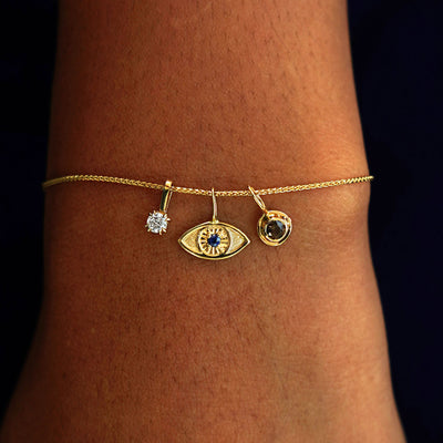A model's wrist wearing a yellow gold Wheat Chain with a Diamond Charm, a Gemstone Evil Eye Charm, and a Coffee Cup Charm