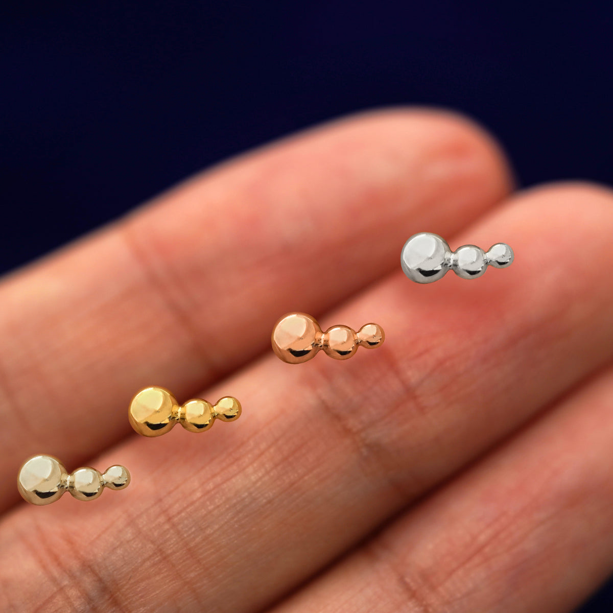 Three versions of the Graduated Ball Earring showing options of yellow, rose, and white gold in between a model's fingers