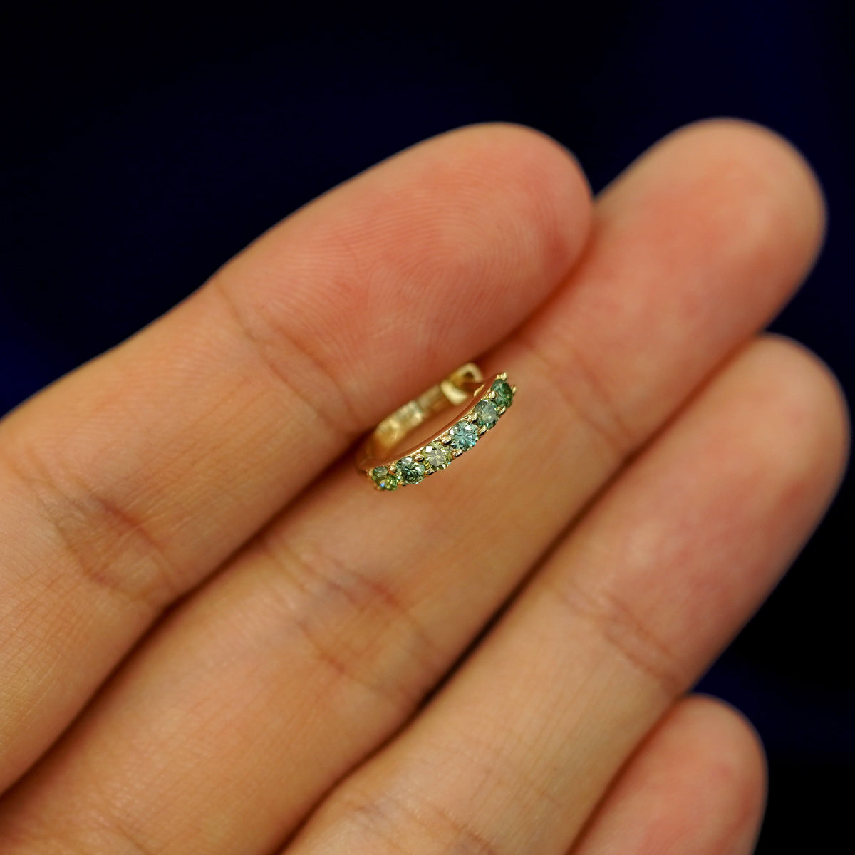 A small Light Green Lab Diamond huggie hoop earring between a model's fingers to show the gems