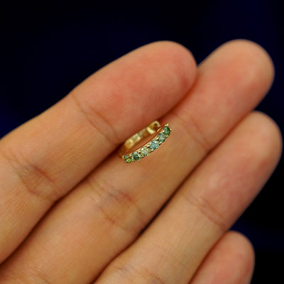 A small Light Green Lab Diamond huggie hoop earring between a model's fingers to show the gems