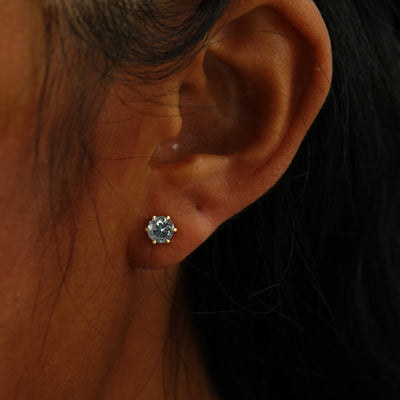 A model's ear wearing a 14k yellow gold grey 5mm Moissanite Earring