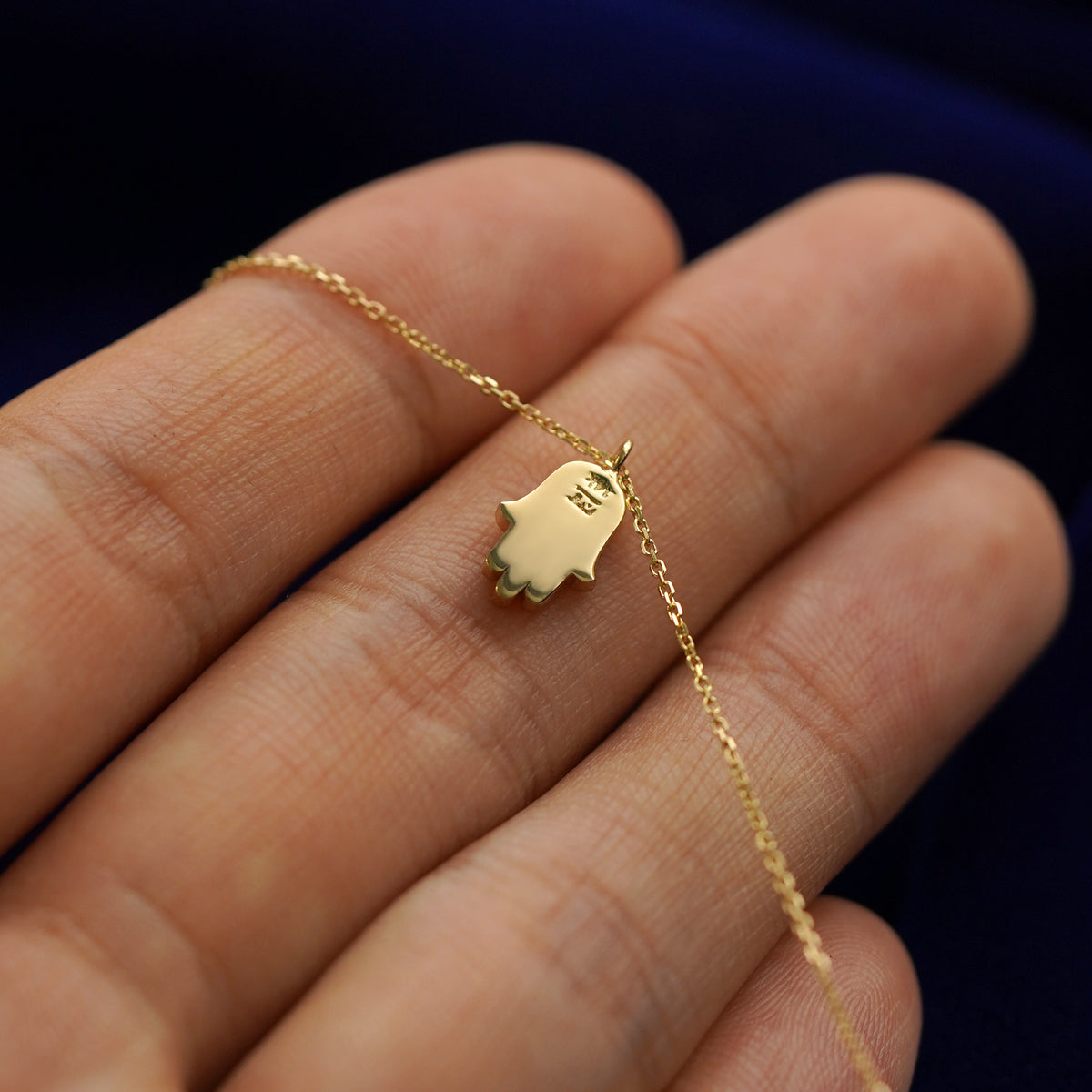 Back side view of a 14k gold hamsa pendant necklace lying across a model's fingertips