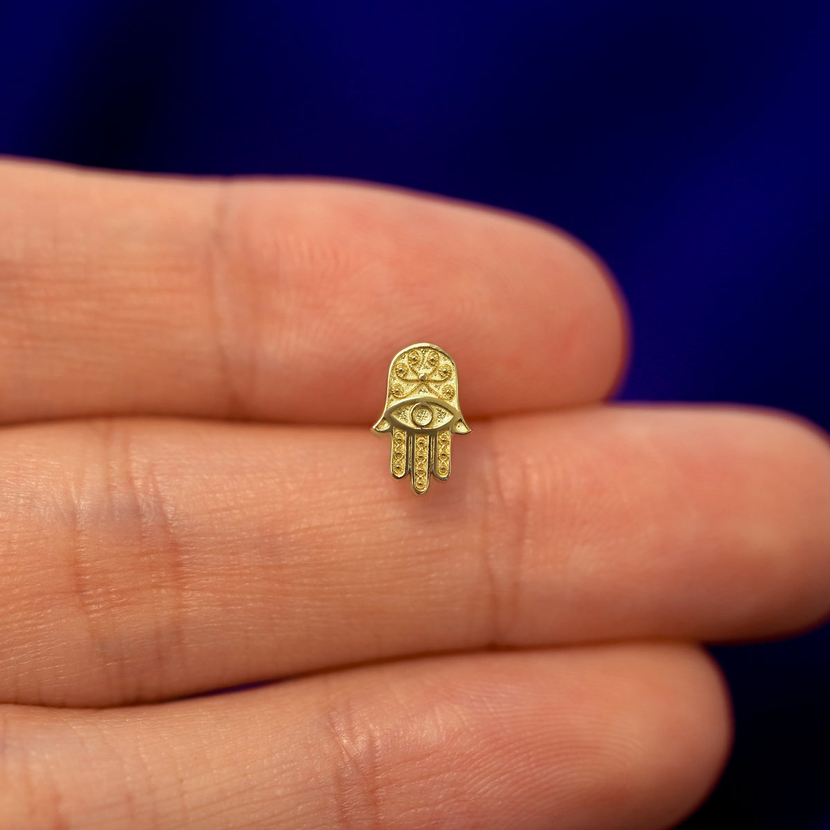 A model holding a solid gold Hamsa stud earring between two fingers