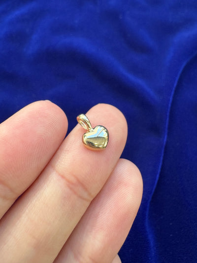 A solid 14k yellow gold heart charm pendant lying face up on a models finger