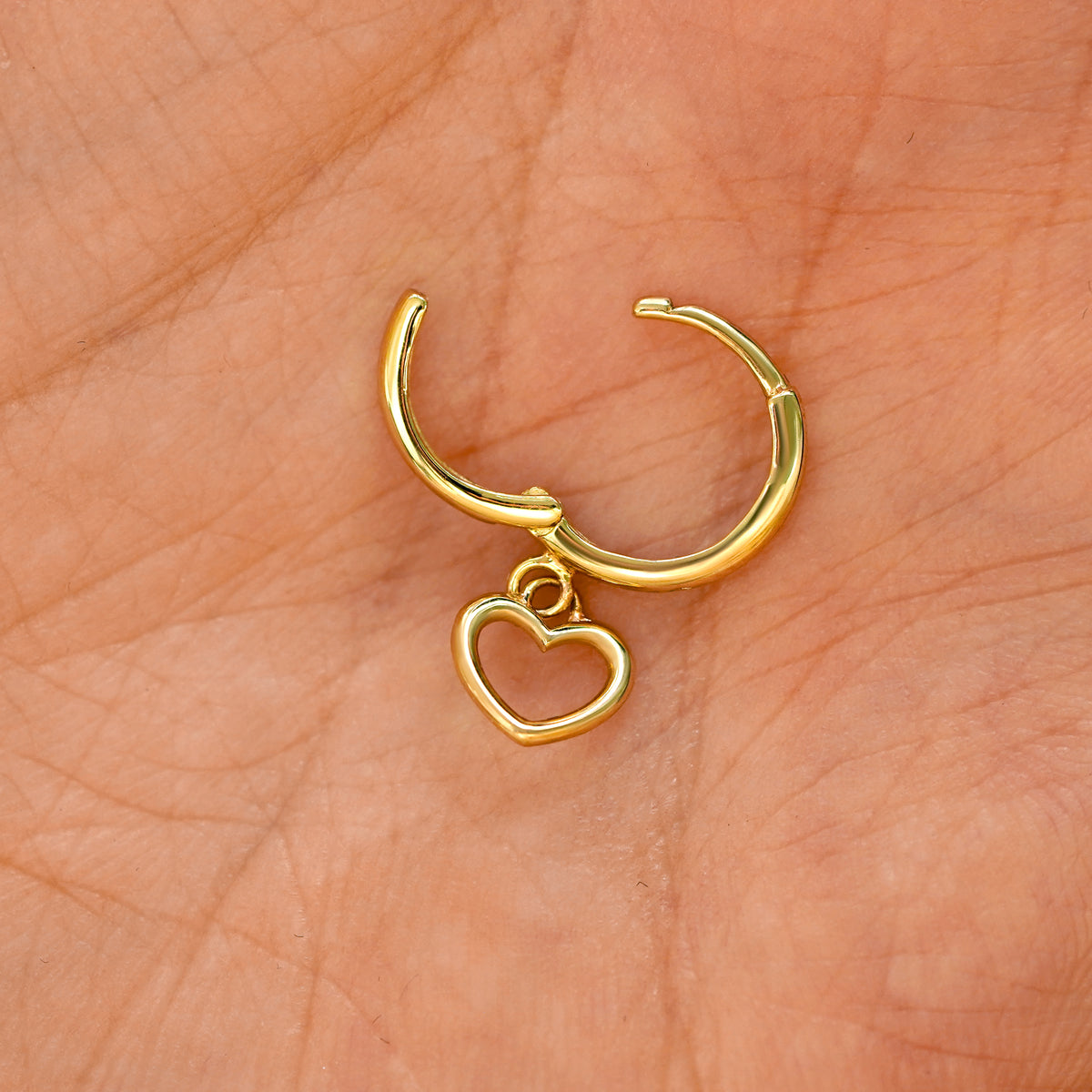 A solid 14k yellow gold Heart Dangle Huggie Hoop Earring open a model's palm