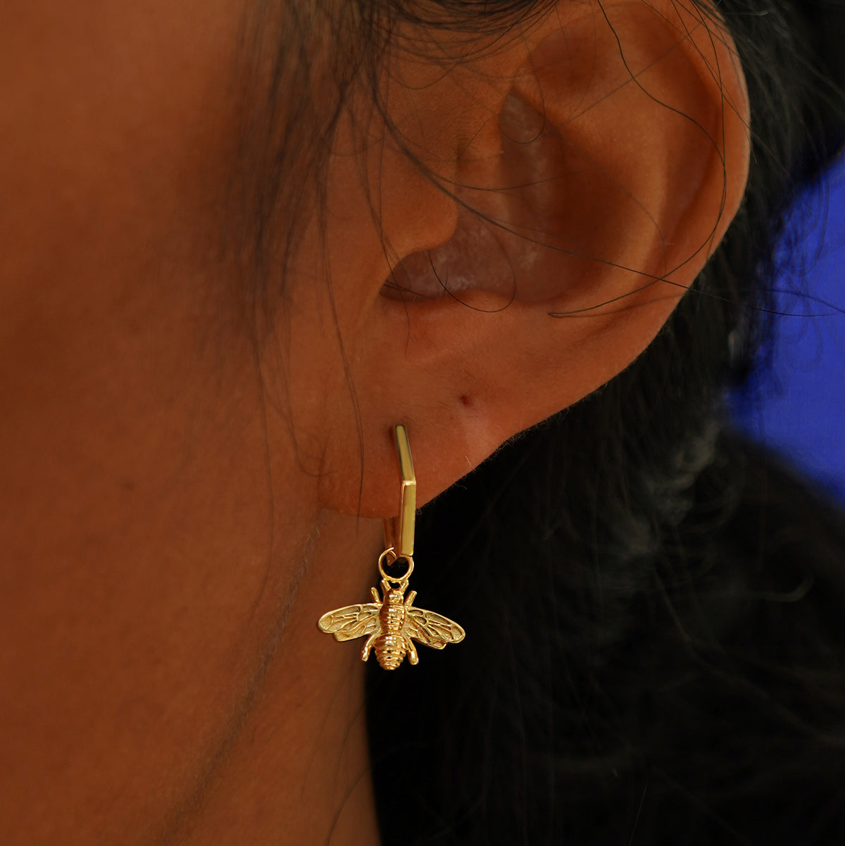 A model's ear wearing a solid yellow gold Hexagon Huggie Hoop with a Bee Charm