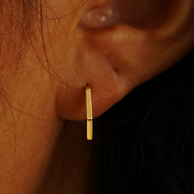 Close up view of a model's ear wearing a solid yellow gold Hexagon Huggie Hoop
