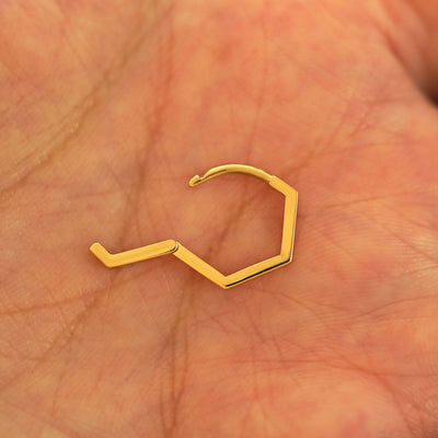 An open 14k yellow gold Hexagon Huggie Hoop resting in a model's palm