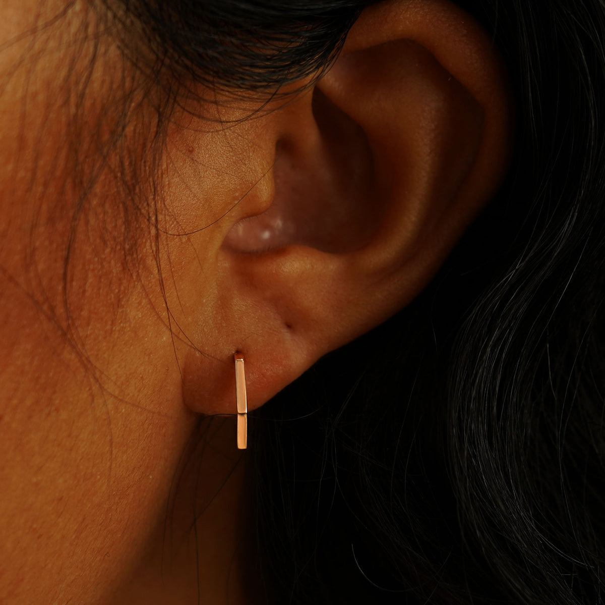 A model's ear wearing a 14 karat rose gold Hexagon Huggie Hoop