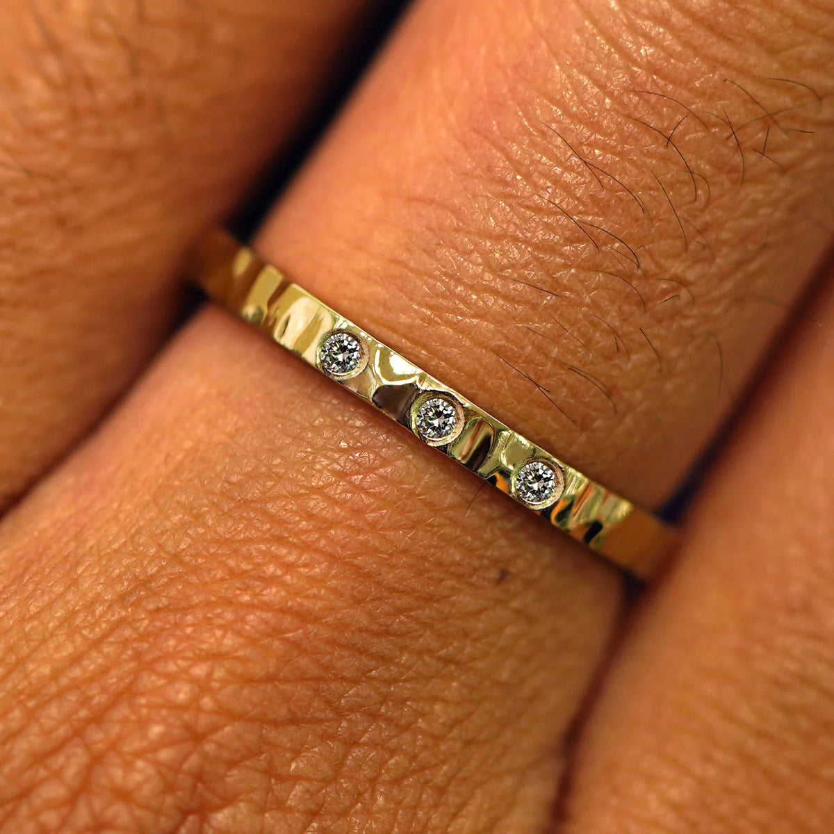 Close up view of a model's fingers wearing a 14k yellow gold Industrial Mirror Band with three diamonds