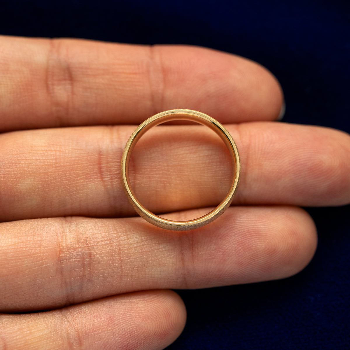 A yellow gold Industrial Matte Band in a model's hand showing the thickness of the band