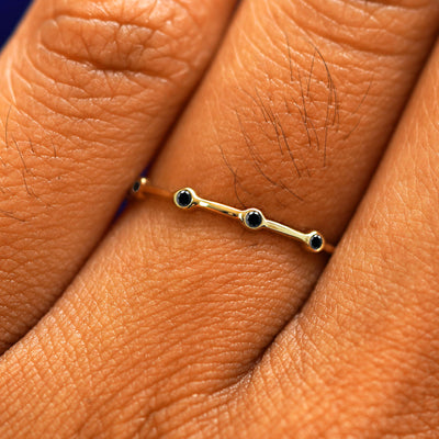 Close up view of a model's fingers wearing a 14k yellow gold Spaced Black Diamond Infinity Ring