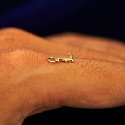 A solid 14k gold Initial Charm for earring in the letter L laying on the back of a model's finger