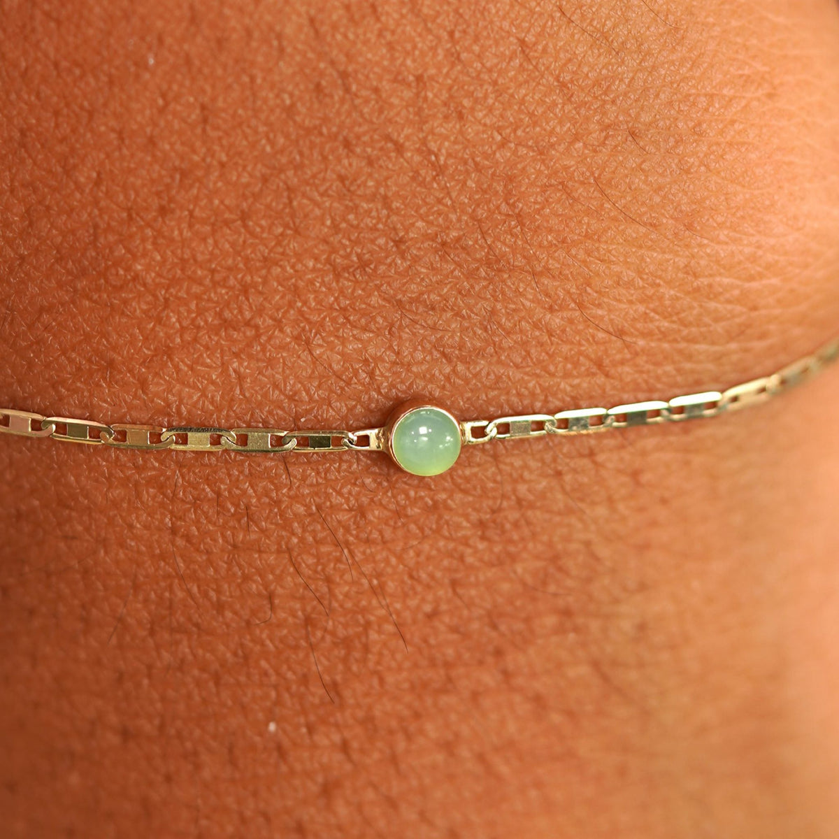 Close up view of a models wrist wearing 14k yellow gold Jade Bracelet