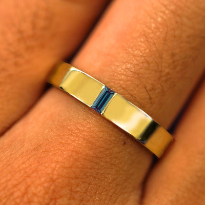 Close up view of a model's hand wearing a solid yellow gold Lab Alexandrite Baguette Band